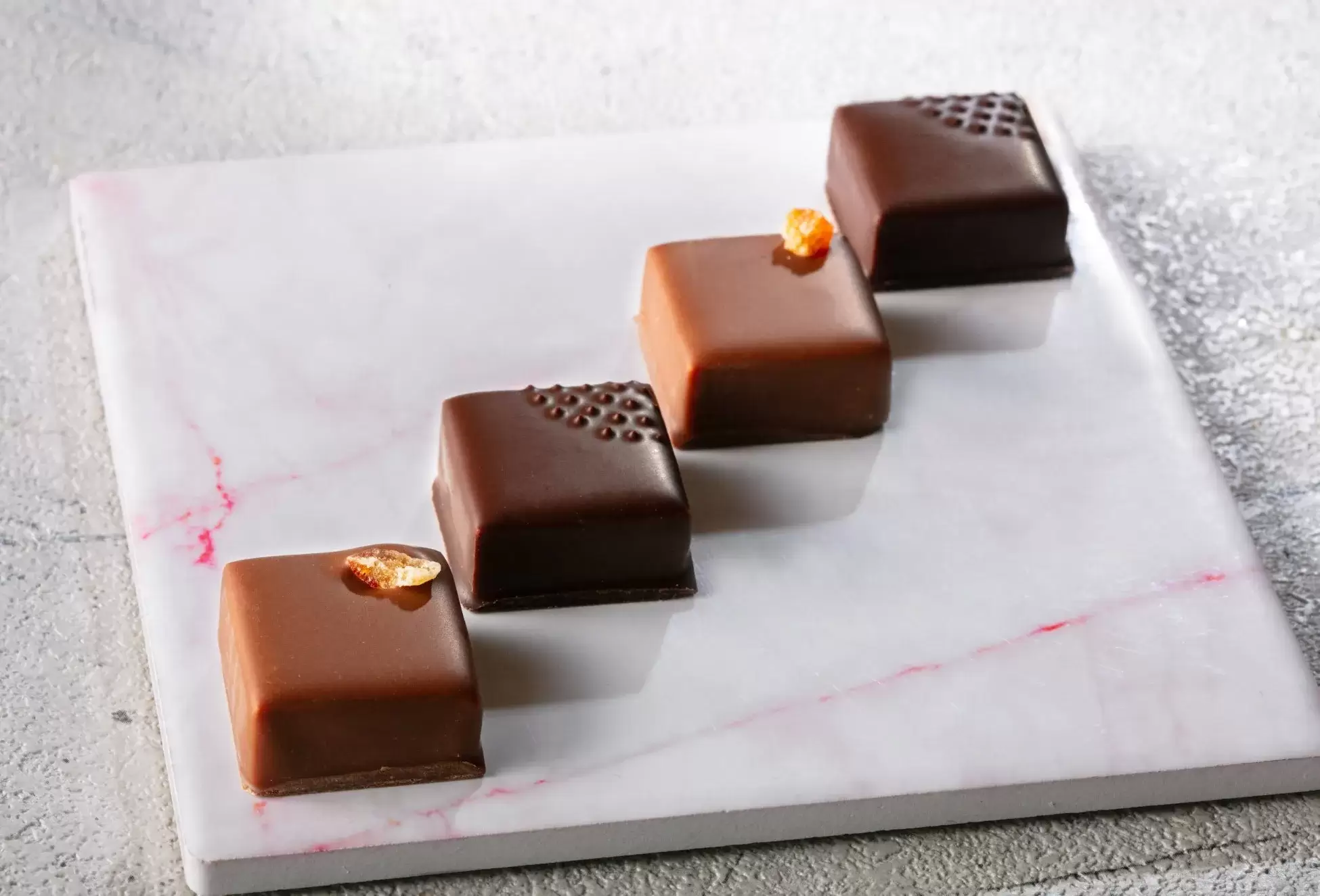大理石の板の上に、4つのチョコレートが並んでいる画像。チョコレートには、それぞれ異なる装飾が施されている。