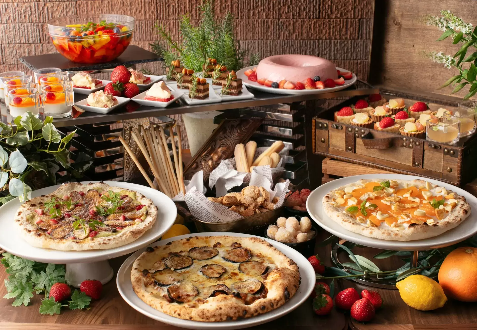 様々なデザートやピザが並べられたビュッフェスタイルの料理の写真。フルーツたっぷりのデザート、ミニケーキ、ピザなど、色とりどりの料理がテーブルに並べられています。