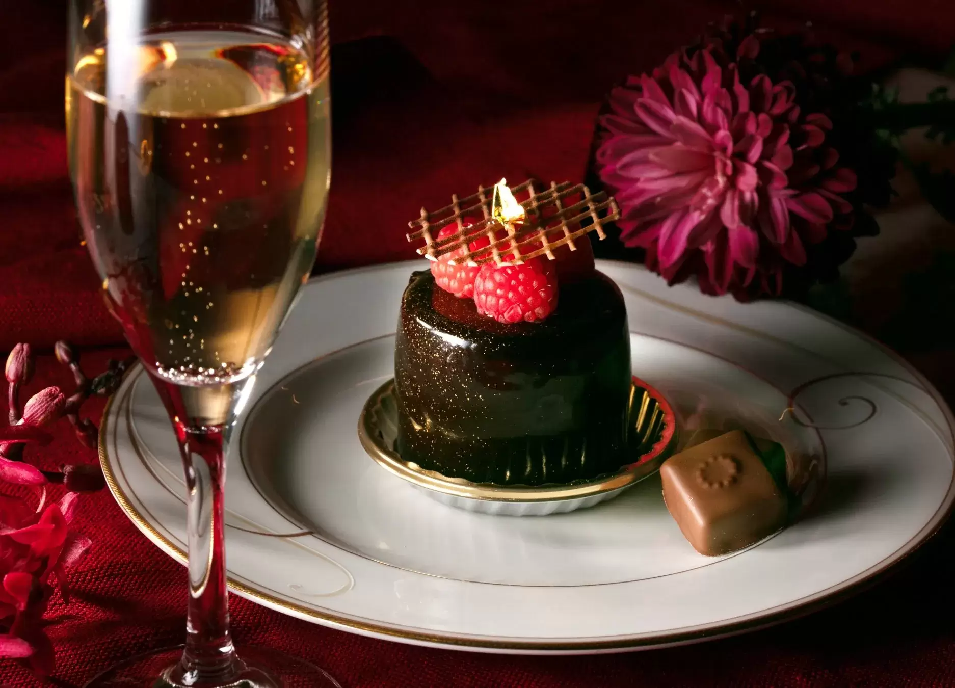 シャンパングラスとチョコレートケーキ、ラズベリー、チョコレート、花が皿に置かれている様子