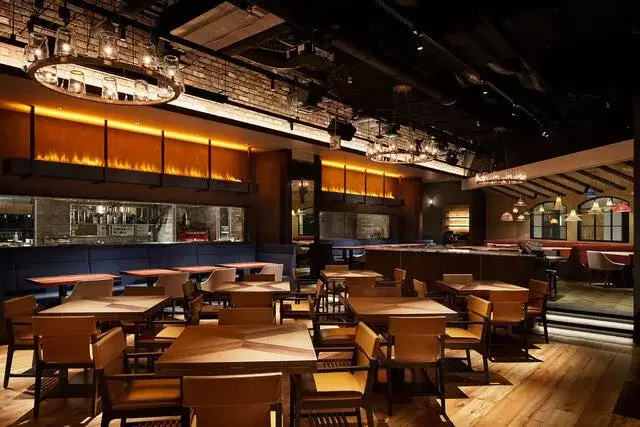 レストランのインテリアの写真。木製のテーブルと椅子が並び、照明が美しい。