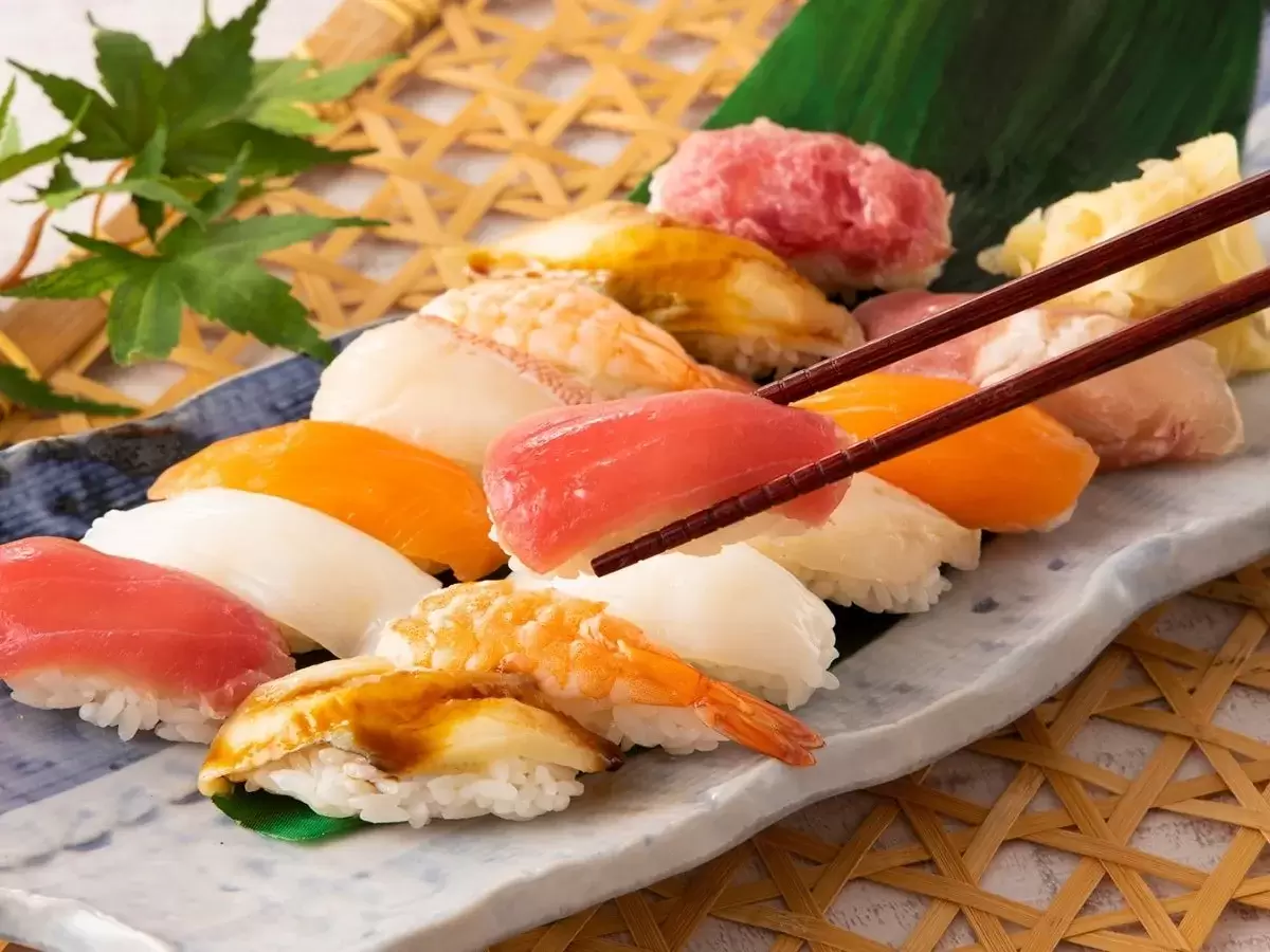 様々なお寿司が並んだ写真。箸でマグロのお寿司が摘まれている。