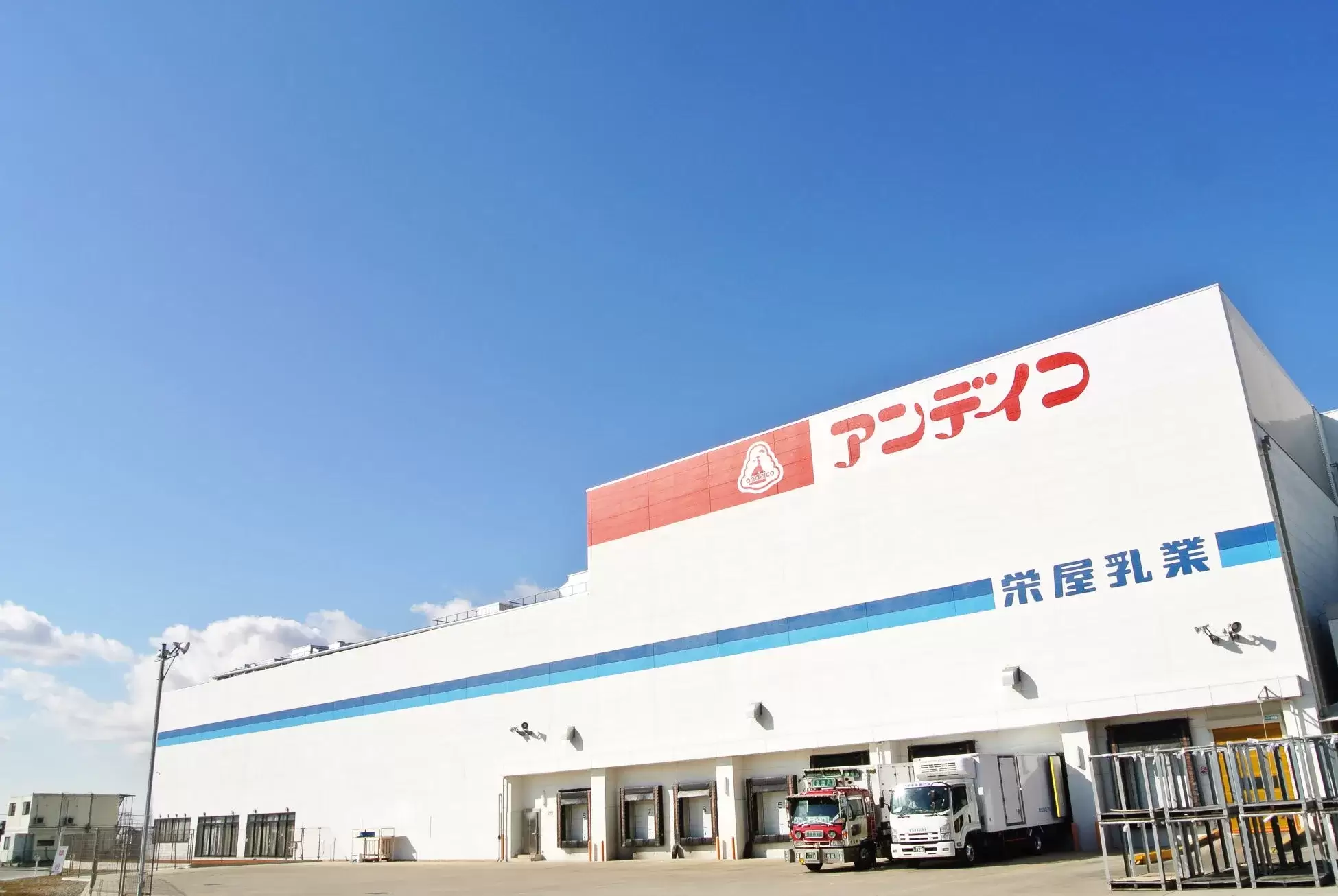 青空の下、白い建物に「アンデコ」と「栄屋乳業」の文字が記された写真。建物の前にはトラックが停まっている。